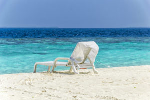 One white beach chair on the beach in front of turquoise water.